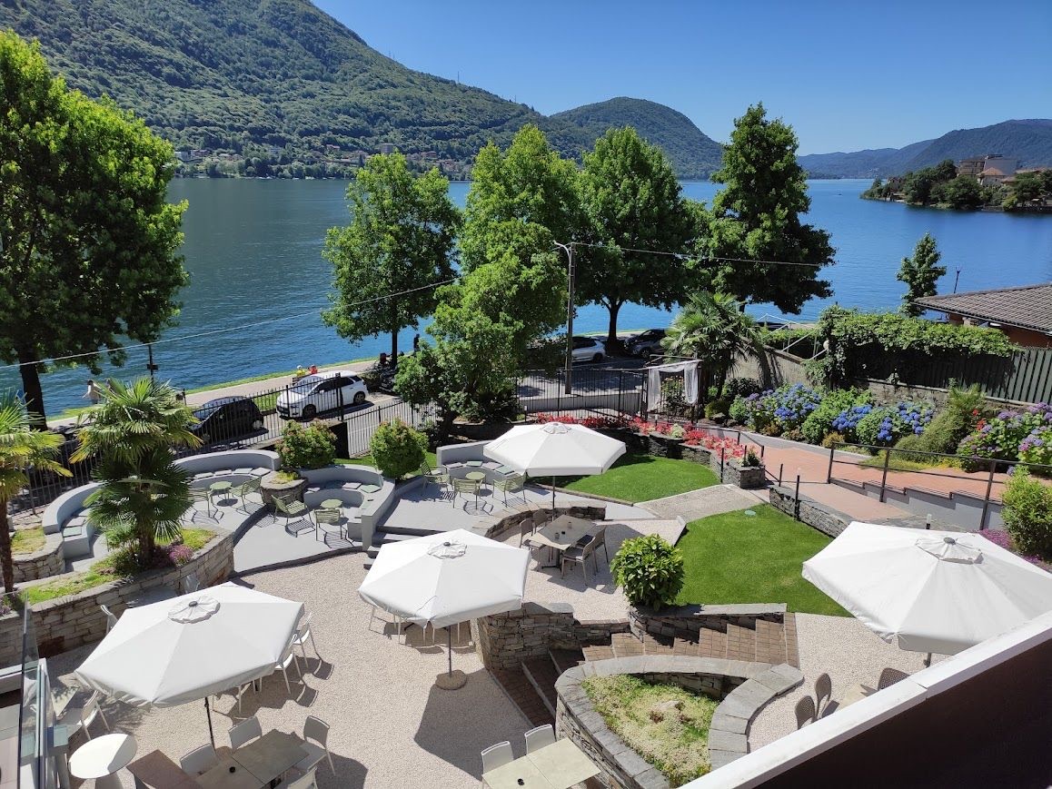 Il giardino con gli ombrelloni bianchi visto dall'alto, con il Lago d'Orta e le montagne sullo sfondo